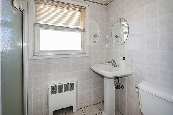 bathroom with tile patterned flooring, toilet, tile walls, radiator, and an enclosed shower