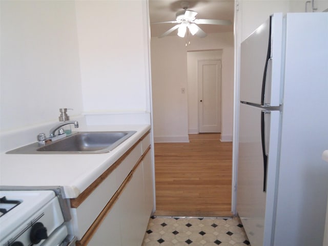 kitchen with ceiling fan, light countertops, freestanding refrigerator, white cabinets, and a sink