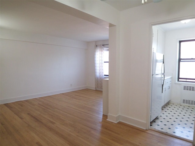 empty room featuring plenty of natural light, radiator, baseboards, and light wood-style floors