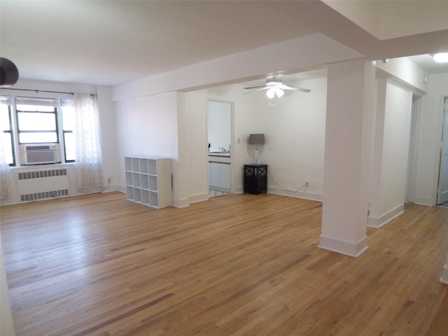 unfurnished living room with cooling unit, baseboards, radiator, and wood finished floors