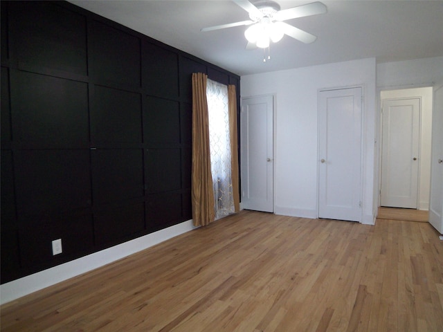 unfurnished bedroom featuring multiple closets, baseboards, light wood-style floors, and a ceiling fan