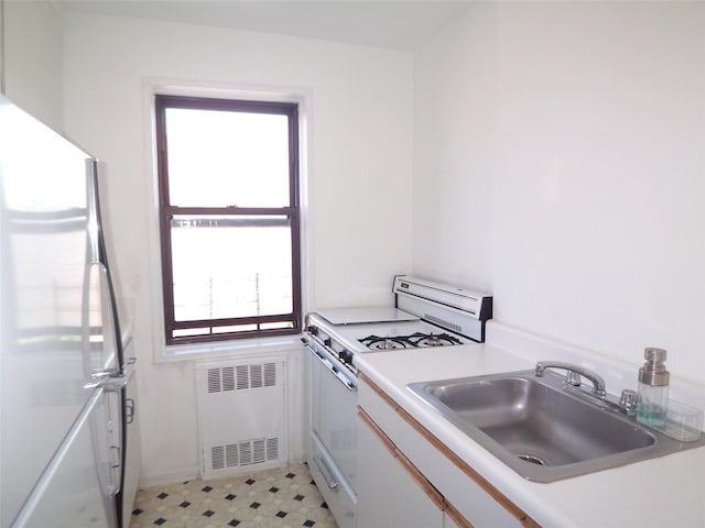 kitchen with gas range gas stove, radiator heating unit, freestanding refrigerator, a sink, and white cabinetry