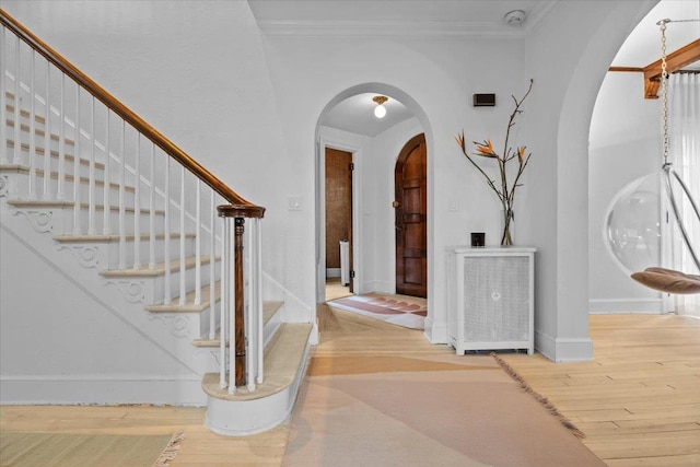 entryway with baseboards, arched walkways, wood finished floors, and ornamental molding