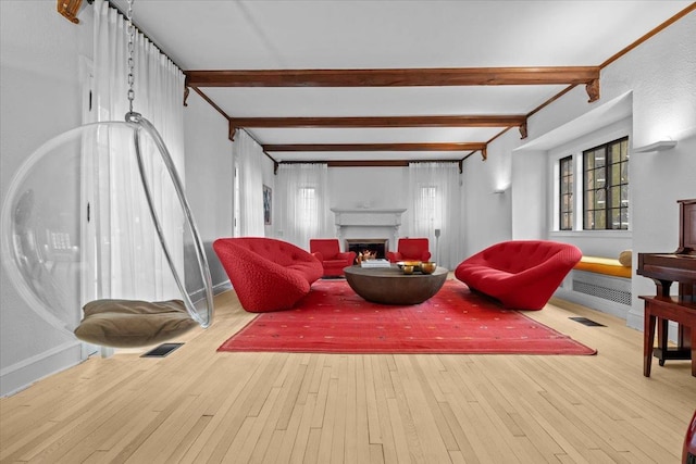 living area featuring a warm lit fireplace, hardwood / wood-style floors, visible vents, and beam ceiling