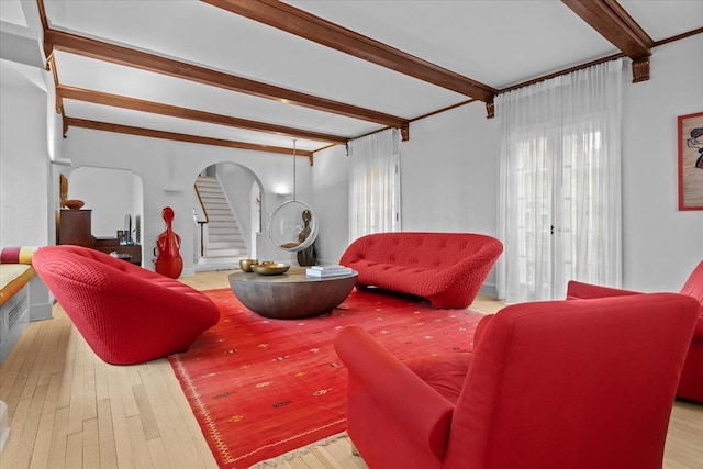 living area featuring wood-type flooring, stairs, arched walkways, and beam ceiling
