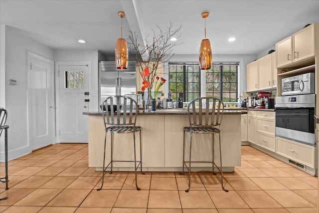 kitchen featuring light tile patterned floors, appliances with stainless steel finishes, a center island, and a kitchen breakfast bar