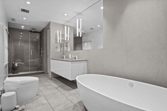 full bathroom with tile walls, vanity, visible vents, a soaking tub, and a shower stall