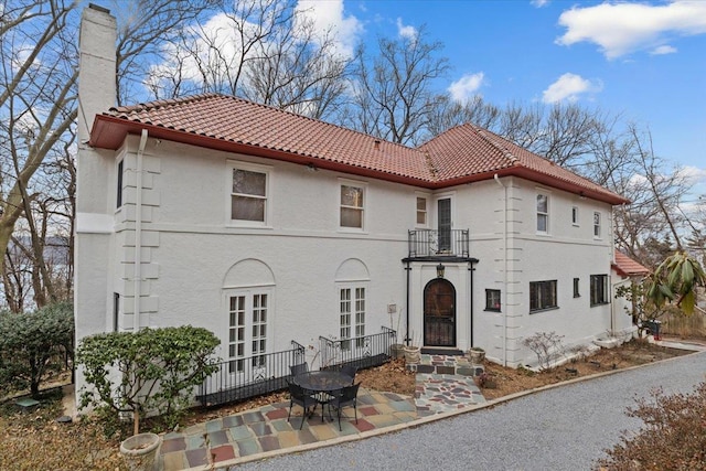 view of front of house featuring a tiled roof, a chimney, a patio, and stucco siding