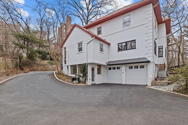 exterior space with a garage, a chimney, central AC unit, and aphalt driveway