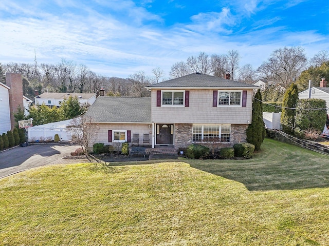 view of front of property featuring aphalt driveway, a chimney, fence, stone siding, and a front lawn