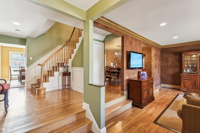 interior space with a decorative wall, light wood-style flooring, wainscoting, a chandelier, and stairs