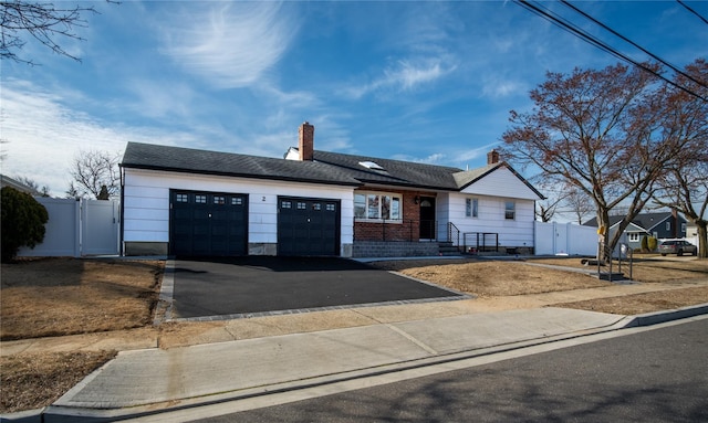 ranch-style home featuring aphalt driveway, a garage, fence, a gate, and a chimney