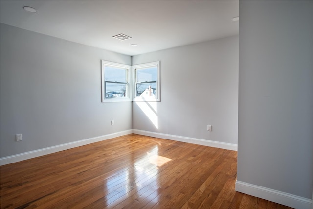 empty room with hardwood / wood-style flooring, visible vents, and baseboards