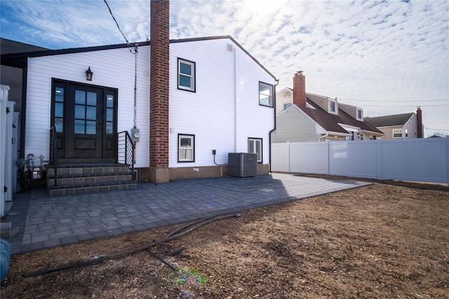 rear view of house with entry steps, central air condition unit, fence, and a patio