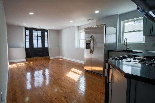 kitchen featuring dark countertops, hardwood / wood-style floors, stainless steel refrigerator with ice dispenser, a sink, and gas stove