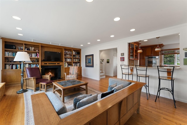 living room with light wood-type flooring, recessed lighting, a fireplace, and crown molding