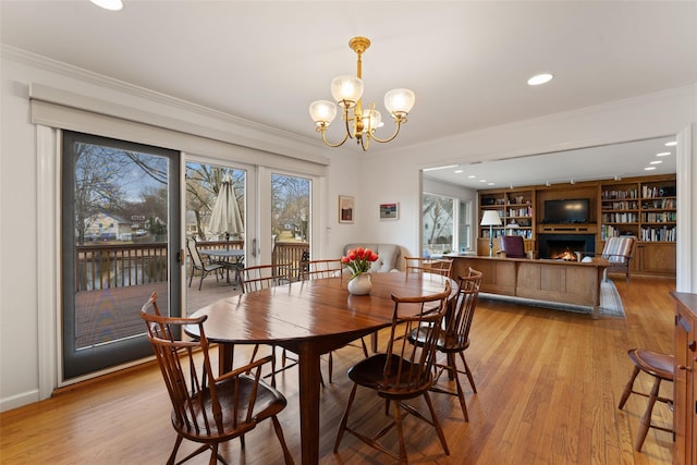 dining space with light wood-style floors, a warm lit fireplace, and crown molding