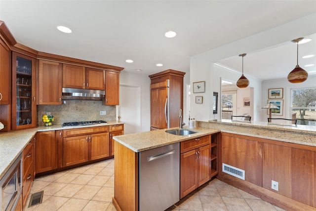 kitchen featuring brown cabinets, visible vents, a sink, built in appliances, and under cabinet range hood