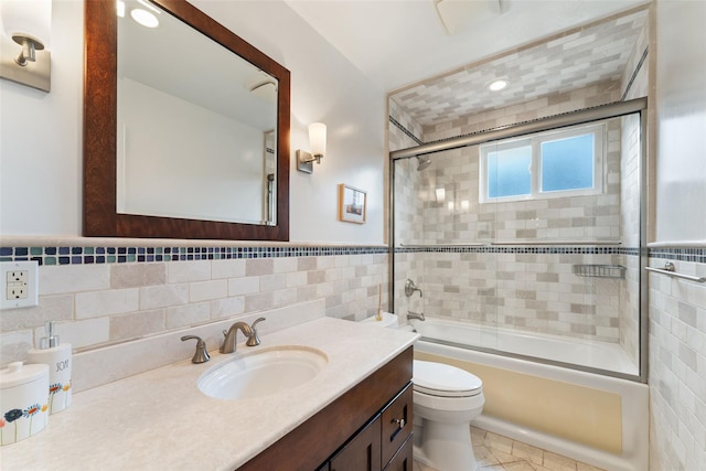 full bath with a wainscoted wall, shower / bath combination with glass door, tile walls, toilet, and vanity