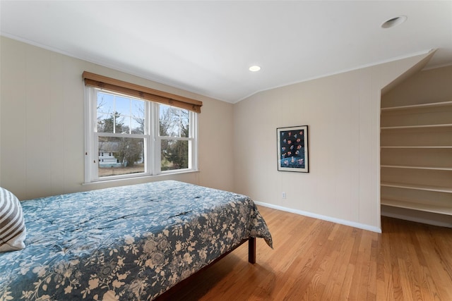 bedroom with light wood finished floors, baseboards, a walk in closet, and ornamental molding