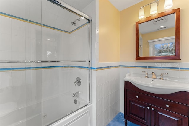 bathroom featuring visible vents, wainscoting, combined bath / shower with glass door, vanity, and tile walls