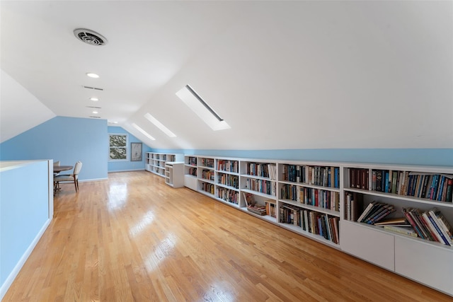 additional living space featuring lofted ceiling with skylight, visible vents, wall of books, and wood finished floors