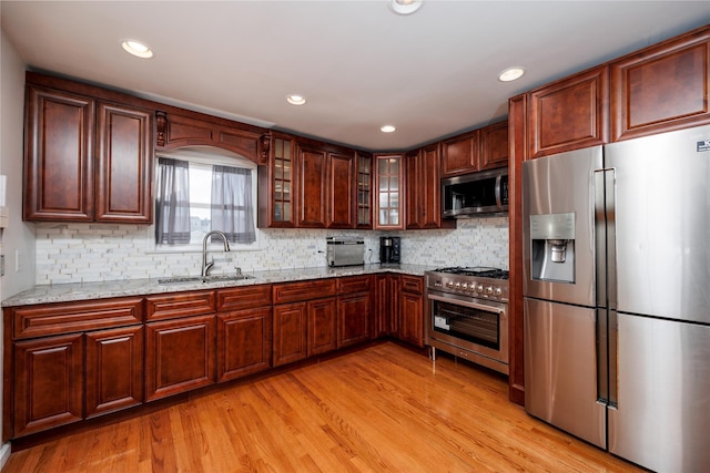 kitchen with light wood-style flooring, glass insert cabinets, light stone counters, stainless steel appliances, and a sink