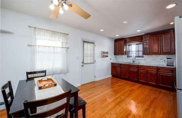 kitchen featuring glass insert cabinets, light wood-type flooring, a sink, and tasteful backsplash