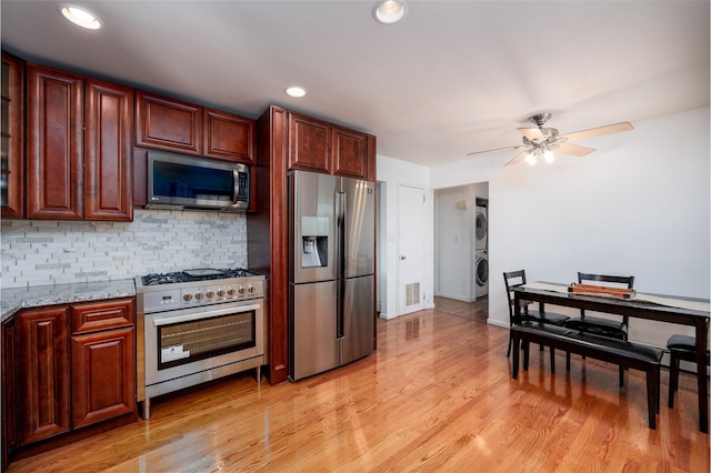 kitchen with stacked washer and dryer, light wood finished floors, decorative backsplash, light stone countertops, and stainless steel appliances