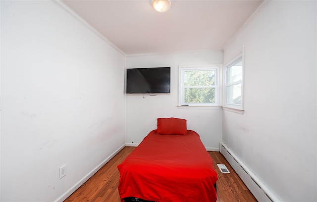 bedroom with crown molding, a baseboard radiator, visible vents, wood finished floors, and baseboards