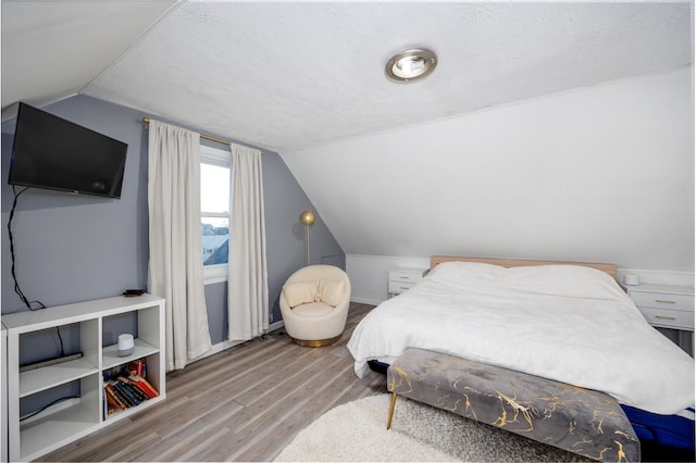 bedroom featuring a textured ceiling, vaulted ceiling, and wood finished floors