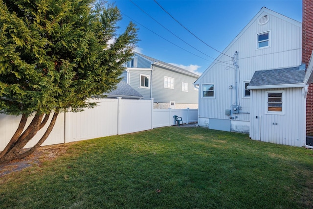 back of house featuring a shingled roof, a lawn, and a fenced backyard