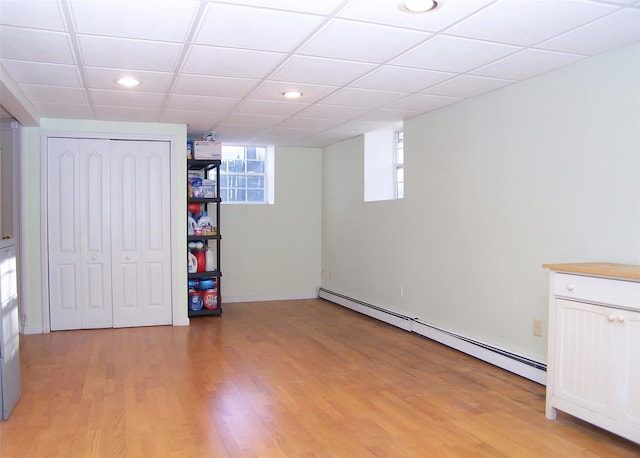 basement with light wood finished floors, baseboard heating, a paneled ceiling, and recessed lighting