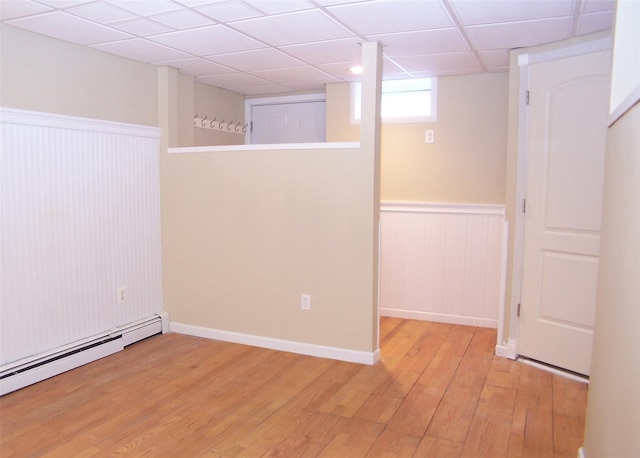 basement with light wood-type flooring, a baseboard radiator, a paneled ceiling, and wainscoting