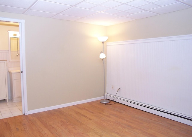 unfurnished room featuring a paneled ceiling, a wainscoted wall, light wood-style flooring, and baseboard heating