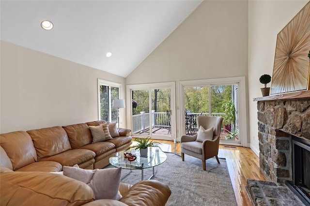 living room with recessed lighting, high vaulted ceiling, a stone fireplace, and light wood-type flooring
