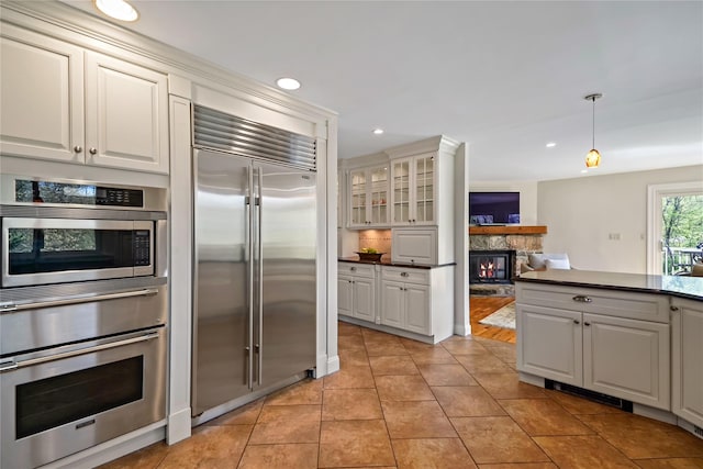 kitchen featuring a stone fireplace, light tile patterned floors, glass insert cabinets, built in appliances, and recessed lighting