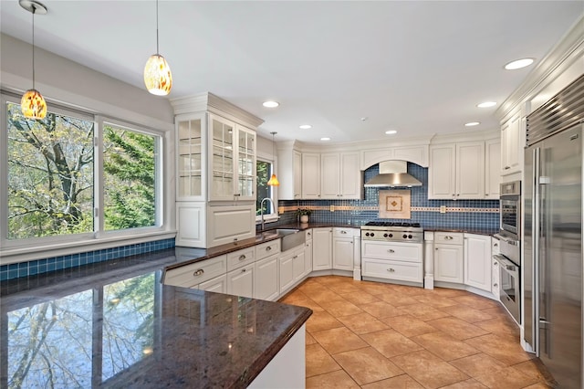 kitchen with wall chimney exhaust hood, a sink, backsplash, decorative light fixtures, and stainless steel appliances