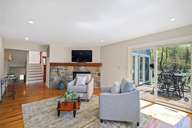 living room featuring visible vents, wood finished floors, a stone fireplace, and stairway