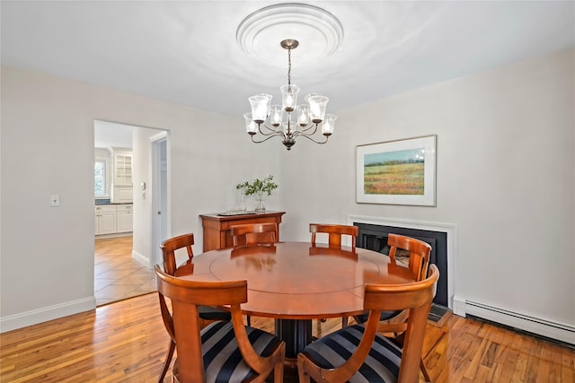 dining area with an inviting chandelier, baseboard heating, light wood finished floors, a fireplace, and baseboards