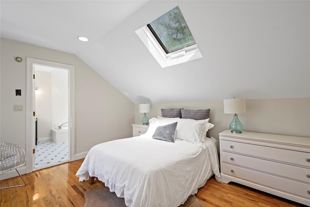 bedroom featuring baseboards, light wood-style flooring, ensuite bath, and vaulted ceiling with skylight