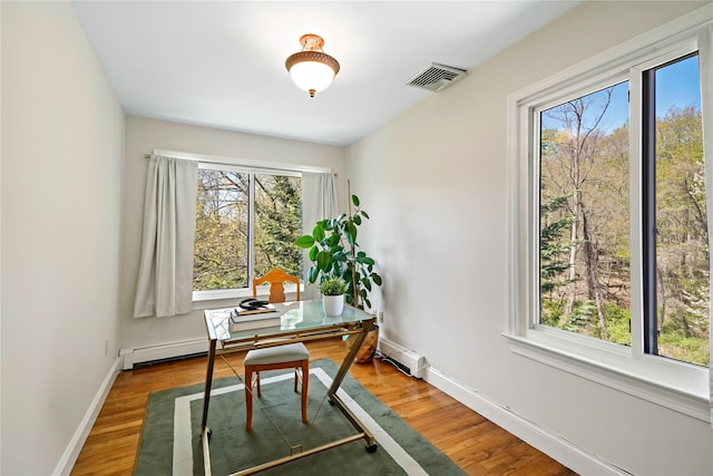 office space with visible vents, a baseboard heating unit, baseboards, and wood finished floors