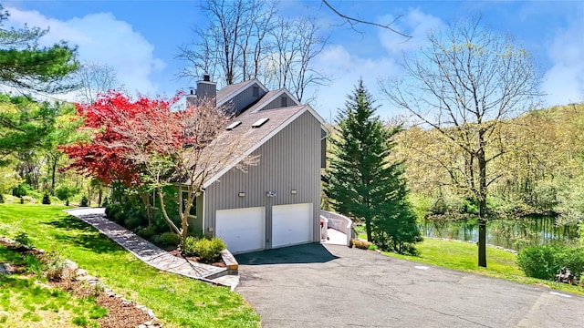 view of property exterior with a garage, a yard, a chimney, a water view, and driveway