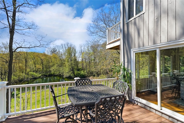 deck featuring a water view, a view of trees, and outdoor dining space