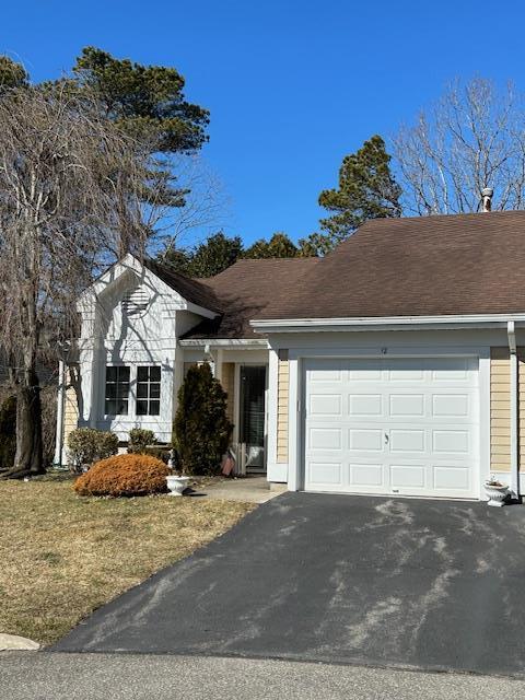 ranch-style house featuring a garage, roof with shingles, and driveway