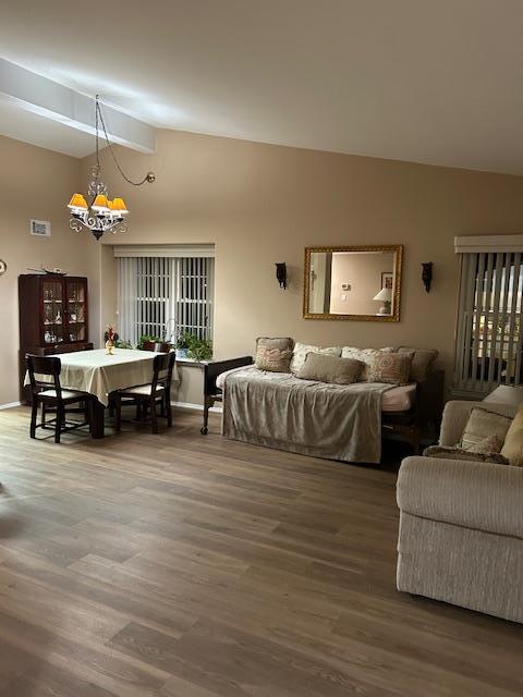 living area with high vaulted ceiling, a notable chandelier, wood finished floors, visible vents, and baseboards