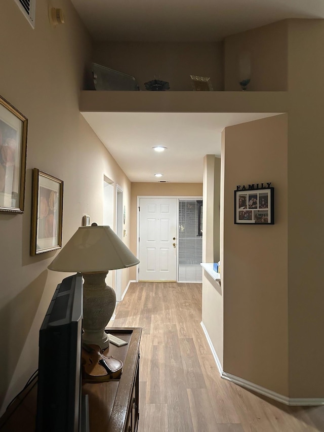 hall with baseboards, visible vents, and light wood finished floors