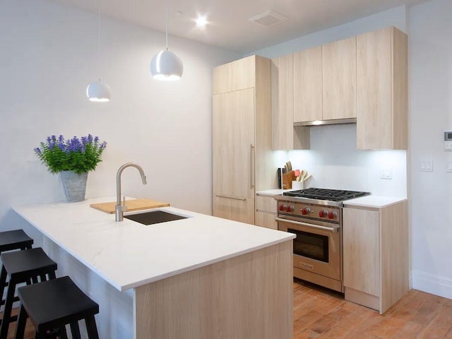 kitchen featuring light brown cabinets, a peninsula, a sink, hanging light fixtures, and premium stove