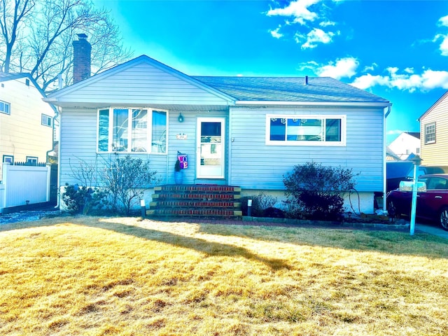 view of front facade featuring entry steps, a chimney, fence, and a front yard