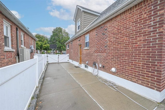 view of side of home with a gate, brick siding, and fence